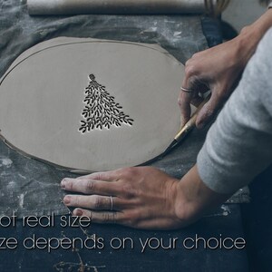 Könnte beinhalten: Eine hellgraue, ovale Tonplatte mit einem in die Oberfläche geschnitzten Baumdesign. Die Platte wird von einer Person bearbeitet. Der Text auf dem Bild lautet "Not real size. Size depends on your choice."