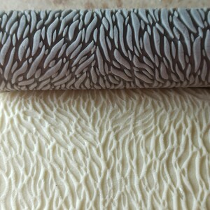 May include: A gray rolling pin with a raised pattern of wavy lines. The rolling pin is used to create a textured pattern on dough.