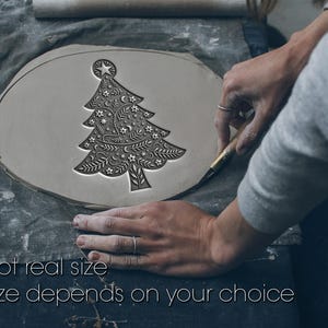 Può includere: Un disegno di albero di Natale in argilla grigia è in fase di intaglio. L'albero presenta intricati dettagli floreali e a stella. Il testo "Not real size" e "Size depends on your choice" è nella parte inferiore dell'immagine.