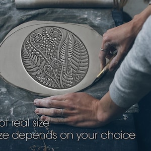 May include: A silver-coloured, oval ceramic piece with a detailed botanical design. The design features ferns and other plant elements within a circular frame. Text reads "Not real size" and "Size depends on your choice".