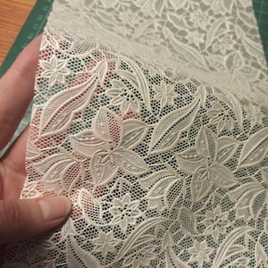 May include: White lace fabric with a floral pattern. The lace has a delicate, intricate design with small flowers and leaves.
