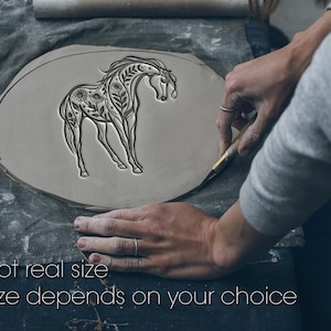 Op de afbeelding: Een plat, ovaalvormig stuk grijze klei met een ingewikkelde, in reliëf gemaakte lijntekening van een paard versierd met bloemmotieven, bladeren en hemelse elementen. De tekst "Not real size" en "Size depends on your choice" is zichtbaar.