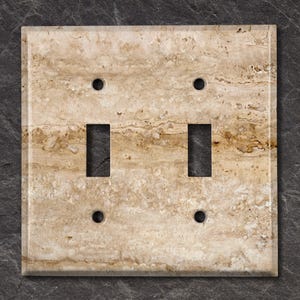 May include: A double light switch cover with a travertine stone design. The cover is beige with brown veins and has a matte finish.