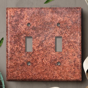 May include: A double light switch cover plate with a rustic, copper-coloured finish. The plate has a textured surface that resembles aged metal.
