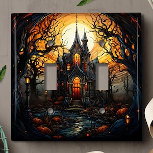 Peut inclure: Une plaque de prise de courant noire avec une illustration d'Halloween effrayante. Une maison sombre de style gothique avec de hautes tours et des fenêtres est entourée d'arbres et de citrouilles. La lune est visible dans le ciel derrière la maison.