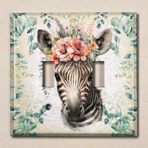 May include: A light switch cover featuring a watercolour illustration of a zebra with a floral crown. The zebra has black and white stripes and the flowers are pink, white, and green. The background is a light green with a watercolour effect.