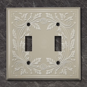 Puede incluir: Una placa de cubierta de interruptor de luz doble con un diseño floral decorativo en acabado níquel cepillado.