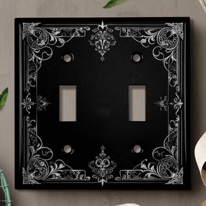 May include: Black light switch cover with a decorative white floral design.