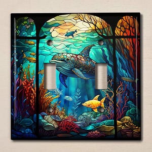 May include: A stained glass style light switch cover featuring a blue whale swimming through a colorful underwater scene with coral, seaweed, and fish.