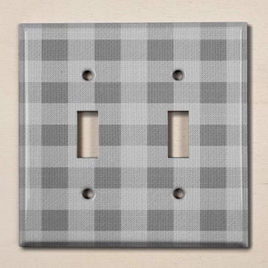 May include: A gray and white checkered light switch cover plate. The plate has two toggle switches and two screw holes.