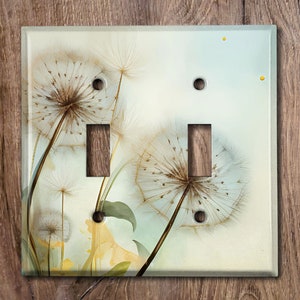 May include: A light switch cover with a dandelion design. The dandelion is white and brown with a light blue background. The switch cover has two toggle switches.