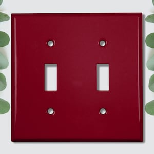 Peut inclure: Une plaque de commutateur à double bascule de couleur rouge foncé. La plaque a une finition lisse et brillante et est en métal.