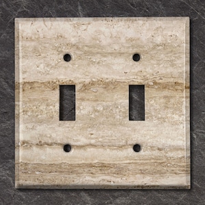 May include: A double light switch cover plate with a travertine stone design. The cover plate is beige with brown streaks and has a textured finish.