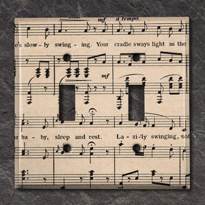 May include: A light switch cover featuring a vintage sheet music design with the lyrics "e's slowly swinging. Your cradle sways light as the... ar ba - by, sleep and rest. Lazi-ly swinging, sof"