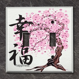 May include: A white light switch cover with a pink and brown cherry blossom tree design. The Japanese characters for "spring" and "happiness" are written on the cover.