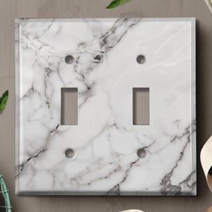May include: White marble light switch cover with two toggle switches. The cover has a realistic marble pattern.