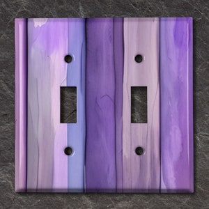 Peut inclure: Plaque de protection pour interrupteur double avec un motif de grain de bois vertical. La plaque présente des nuances de violet, de lavande et de blanc. Elle comporte deux ouvertures pour interrupteurs et quatre trous de vis.