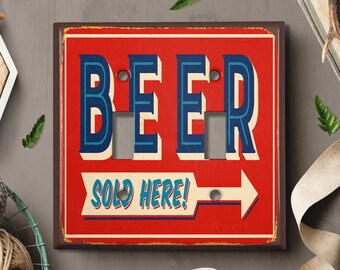 May include: A red and white light switch cover with the word "BEER" in blue and white letters and the text "SOLD HERE!" with an arrow pointing to the right.