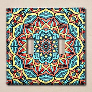 May include: A light switch cover with a colorful mandala design. The mandala features blue, yellow, red, and orange colors. The design is intricate and detailed.