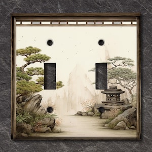 May include: A light switch cover with a Japanese garden scene. The cover features a white background with a gray stone pagoda, green trees, and a mountain range in the background.