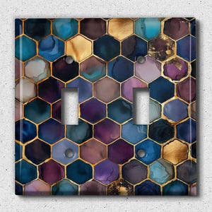 May include: A decorative double light switch cover with a hexagonal pattern. The design features a mosaic of blue, purple, gold, and teal shapes with gold outlines. The cover has two switch openings and silver screws.