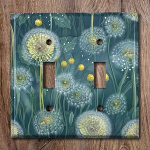 May include: A light blue and green light switch cover with a dandelion pattern. The dandelions are white with yellow centers and are scattered across the cover.