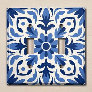 May include: A white light switch cover with a blue and white geometric pattern. The pattern features stylised flowers and leaves.