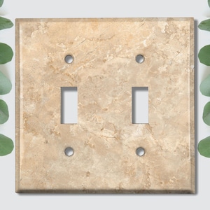 May include: A light brown, textured, rectangular light switch plate with two toggle switches and two screw holes.