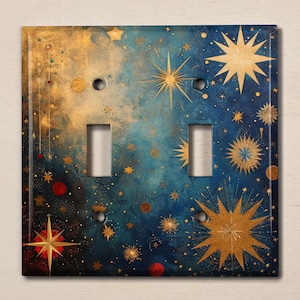 May include: A decorative double light switch cover with a celestial design. The cover features a dark blue background with gold and red stars, and a textured, artistic finish. The cover has two rectangular switch openings and two screw holes.
