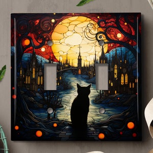 May include: A black cat sits in front of a stained glass window depicting a city with a full moon in the background. The window is framed in black and has a light switch plate design.