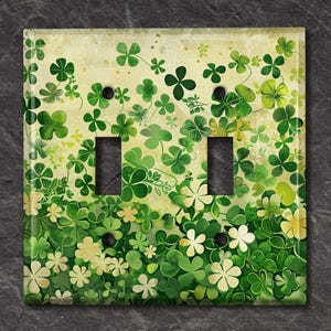 May include: A decorative light switch cover featuring a vibrant design of green shamrocks and clovers on a cream-colored background. The cover has two switch openings and is perfect for adding a touch of Irish charm to any room.