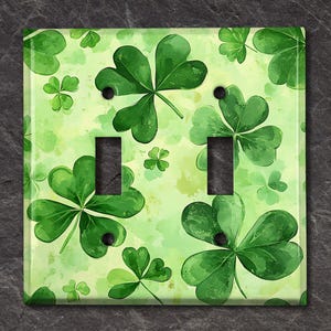 May include: A light green light switch cover with a watercolor pattern of shamrocks. The shamrocks are green with white outlines and are scattered across the cover.