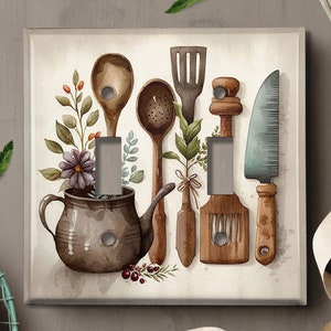May include: A light switch cover with a watercolor illustration of kitchen utensils, including a wooden spoon, a ladle, a spatula, a knife, and a teapot. The illustration is surrounded by green leaves and purple flowers.