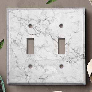 May include: White marble light switch cover with two toggle switches and two outlet holes.