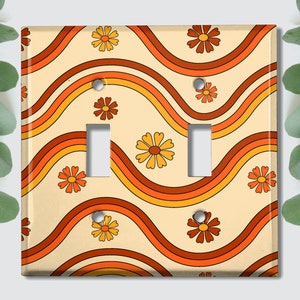May include: A light switch cover with a retro design featuring orange, yellow, and brown wavy lines and orange daisy flowers.