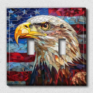 May include: A decorative double light switch cover featuring a detailed mosaic-style image of a bald eagle's head against a backdrop of the American flag. The eagle has a yellow beak and piercing eyes, with a background of red, white, and blue.