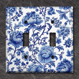 May include: A white light switch cover with a blue and white floral pattern. The pattern features blue flowers and leaves on a white background.