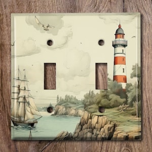 May include: A light switch cover featuring a vintage illustration of a lighthouse, a sailboat, and a rocky coastline. The switch cover is white with two toggle switches.