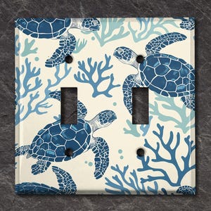 May include: A light switch cover with a white background and a blue and white pattern of sea turtles and coral.