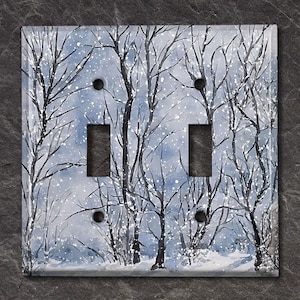 May include: A double light switch cover featuring a winter forest scene. The design showcases bare trees against a snowy, blue-toned backdrop. The cover has two toggle switch openings and two screw holes.
