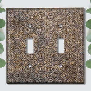 Puede incluir: Una placa de interruptor doble con un patrón geométrico decorativo en relieve en tonos marrones y dorados.