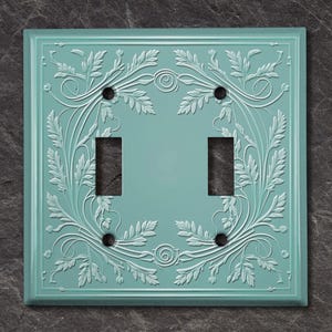Puede incluir: Una placa de interruptor doble de color azul claro con un diseño floral en relieve.
