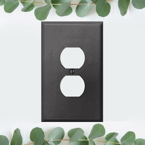 May include: Black outlet cover plate with a single outlet opening. The cover plate is made of metal and has a matte finish.