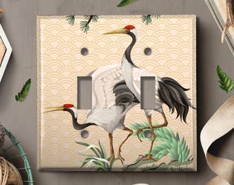 May include: A light switch cover with a beige background featuring two white and black cranes with red accents. The background has a pattern of overlapping beige and white semi-circles.