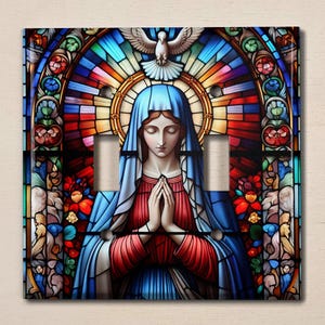 May include: A stained glass light switch cover featuring a depiction of the Virgin Mary praying with a dove above her head. The stained glass design is colorful and intricate, with shades of blue, red, yellow, and green.