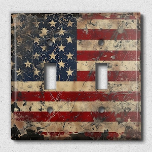 May include: A double light switch cover with a distressed American flag design. The flag is red, white, and blue with a faded and worn look.