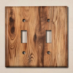May include: A double light switch cover with a rustic woodgrain design. The cover is brown with a light brown woodgrain pattern.