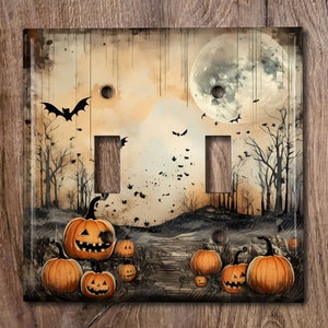May include: A double light switch cover with a Halloween theme. The design features a full moon, bats, and a path lined with jack-o'-lanterns in a spooky forest setting.