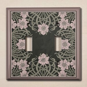 May include: A light brown double light switch cover with a floral design. The design features pink flowers and green leaves on a dark gray background.