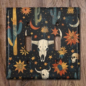 May include: A black light switch cover with a repeating pattern of cacti, stars, skulls, and flowers. The pattern is in shades of yellow, orange, red, blue, and green.